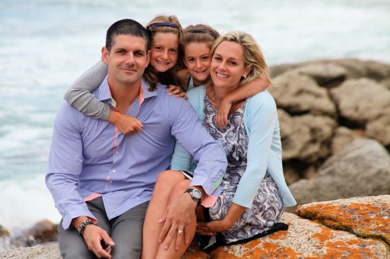 A family is posing for a picture while sitting on a rock near the ocean.