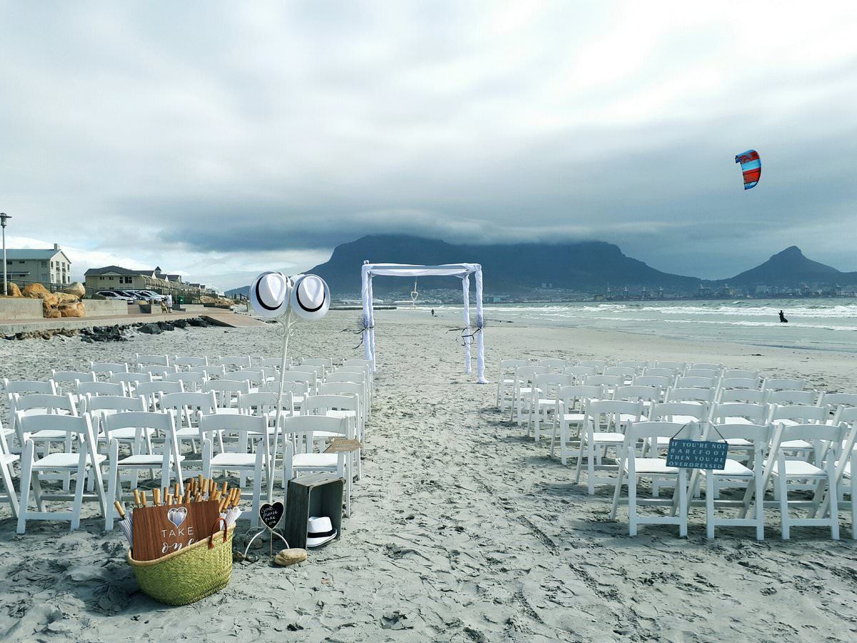 A row of white chairs are lined up on a beach.