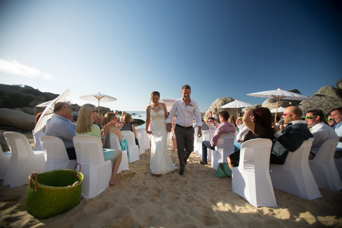 A bride and groom are walking down the aisle at a beach wedding