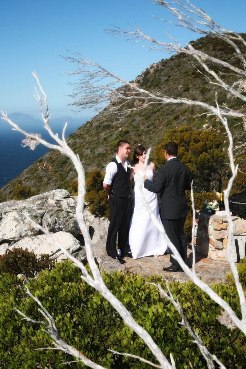 A bride and groom are standing next to each other on top of a mountain.