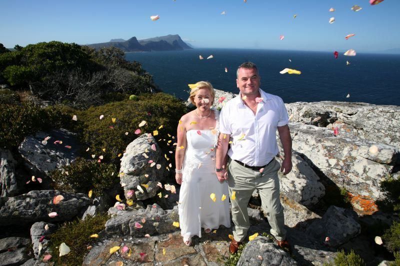 A bride and groom are standing on a rocky cliff overlooking the ocean.