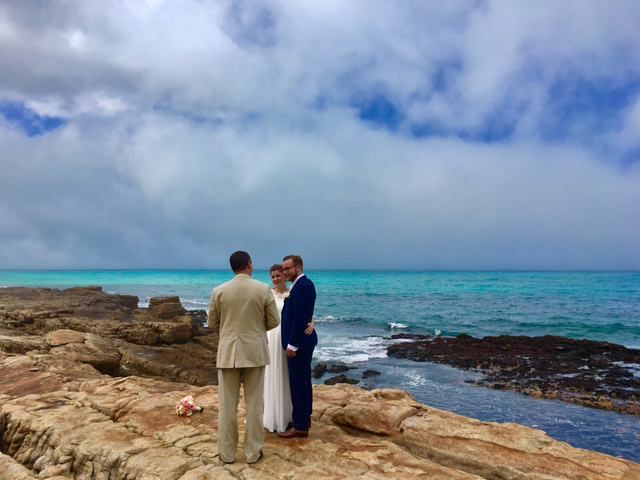 A bride and groom are standing on a rocky cliff overlooking the ocean.