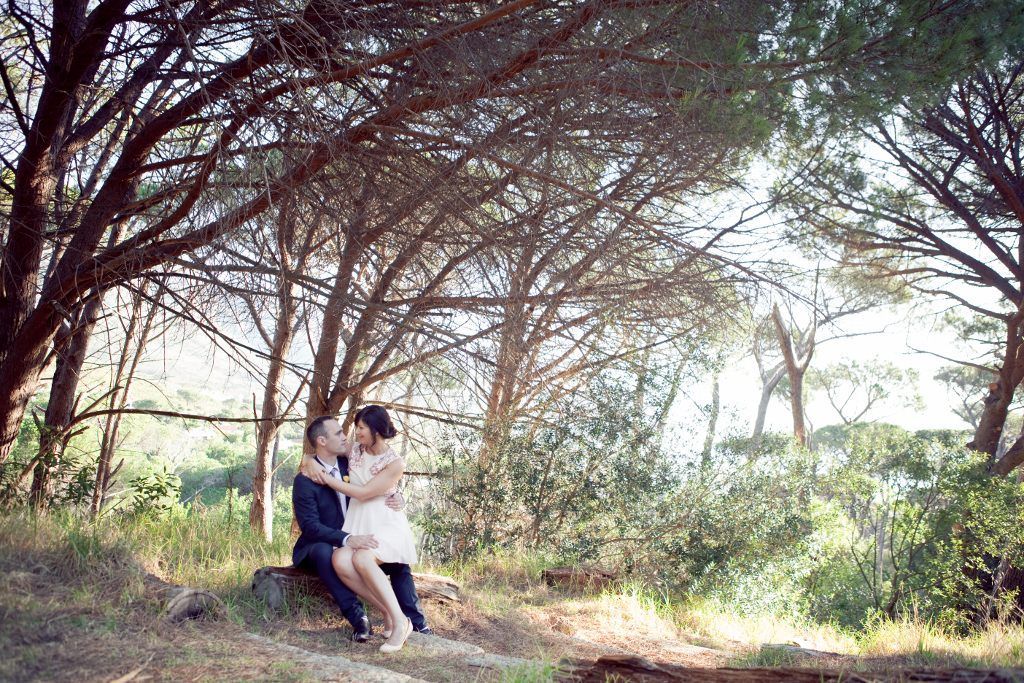 A man and a woman are sitting under a tree in the woods.