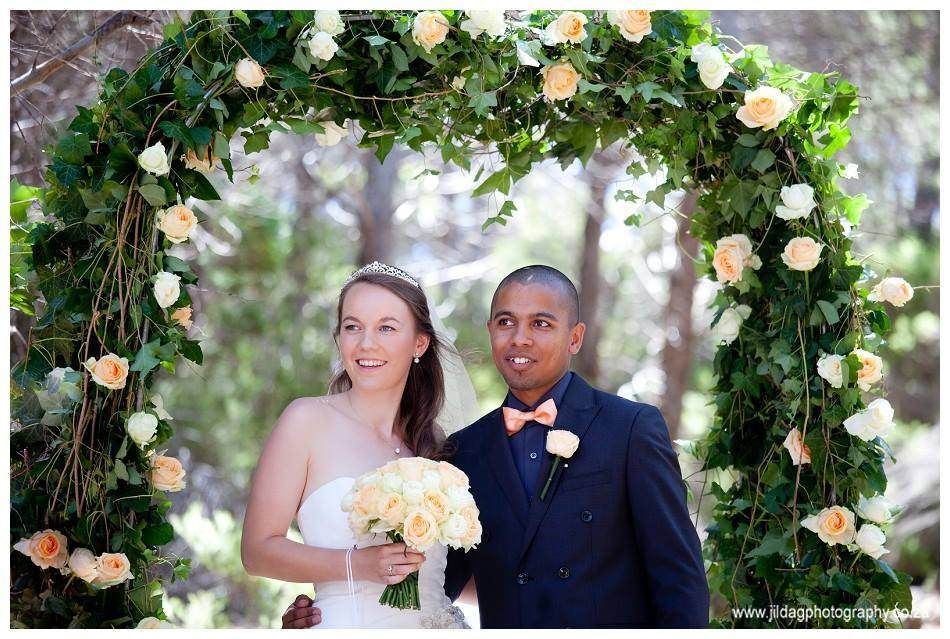 A bride and groom are standing under a flower arch.