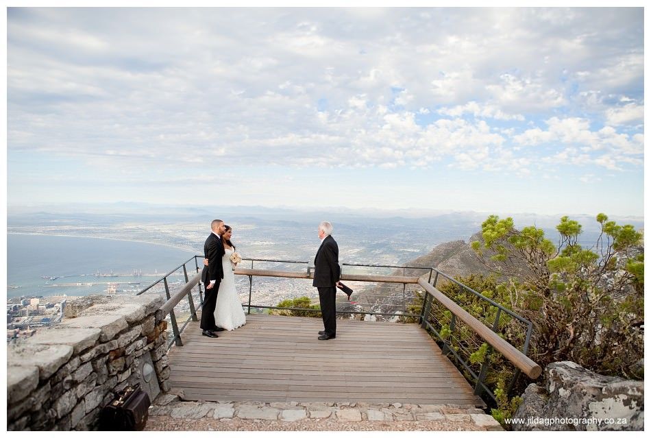 A bride and groom are standing on a balcony overlooking the ocean.