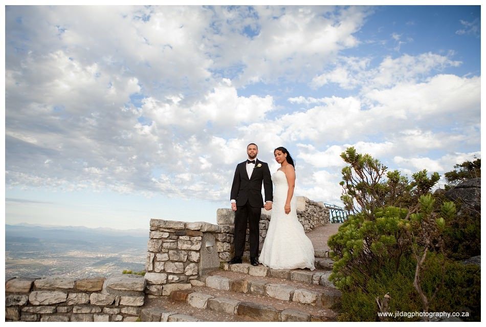 A bride and groom are posing for a picture on top of a mountain.