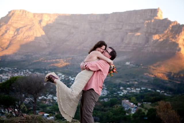 A man is holding a woman in his arms in front of a mountain.