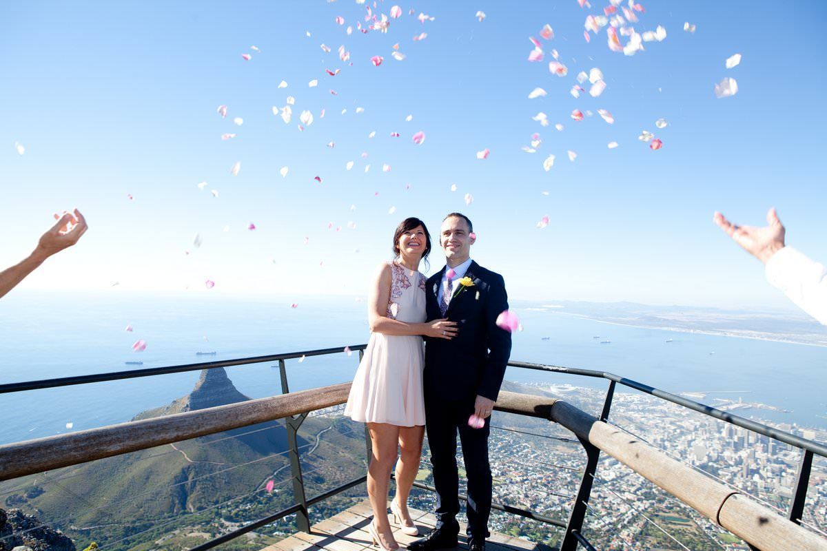A bride and groom are standing on top of a mountain with confetti being thrown in the air.