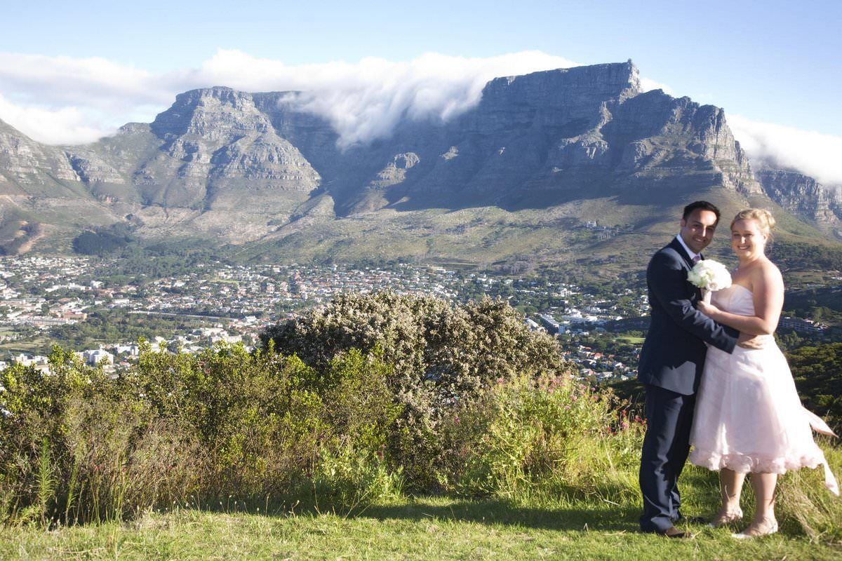 A bride and groom are posing for a picture with a mountain in the background.