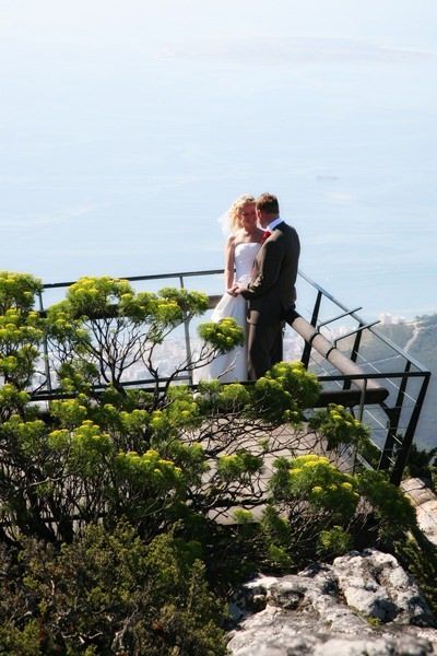 A bride and groom are standing on a balcony overlooking the ocean.