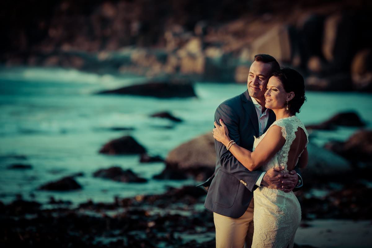 A bride and groom are posing for a picture on the beach.