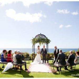 A bride and groom are getting married in front of a gazebo overlooking the ocean.