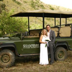 A bride and groom pose in front of a shamwari vehicle