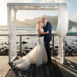 A bride and groom kissing in front of the ocean