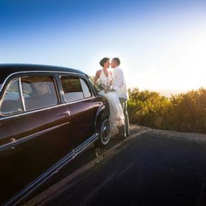 A bride and groom are kissing in front of a car.