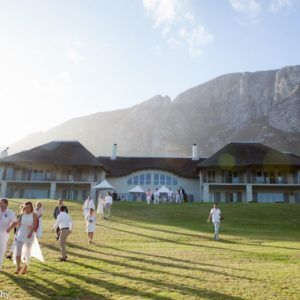 A group of people walking in front of a large house with mountains in the background