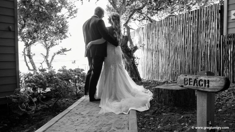 A black and white photo of a bride and groom standing next to a beach sign.