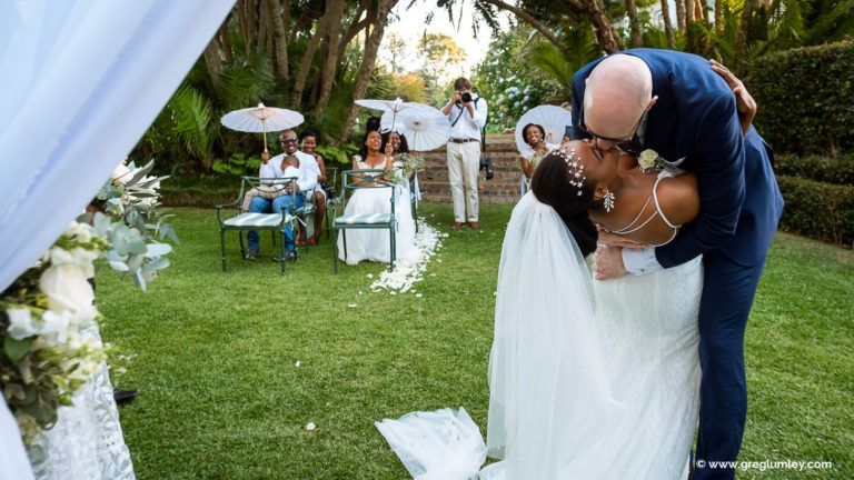 A bride and groom are kissing during their wedding ceremony.
