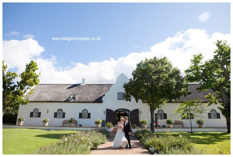 A bride and groom are walking in front of a white building