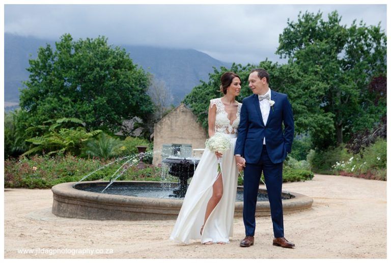 A bride and groom are posing for a picture in front of a fountain.