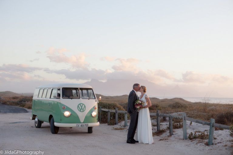 A bride and groom are kissing in front of a vw van.