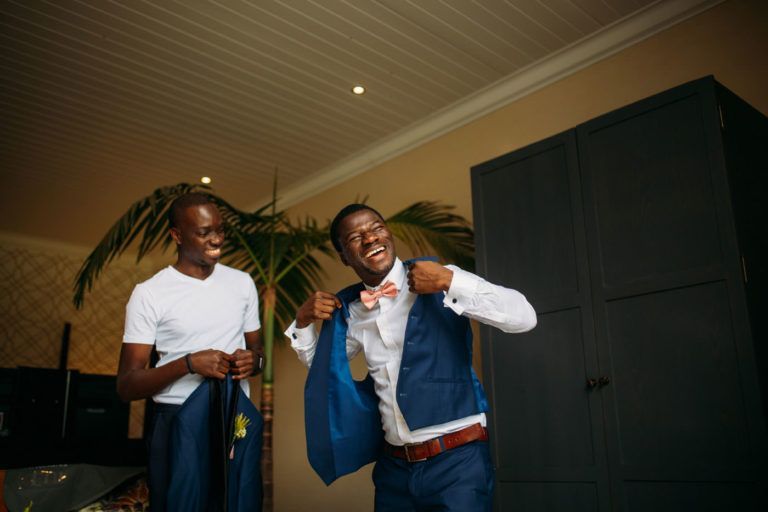 Two men are standing next to each other in a room getting ready for a wedding.