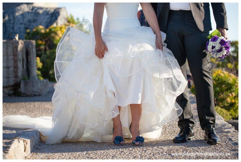 A bride and groom are posing for a picture while the bride is holding her dress.