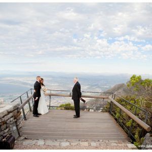 A bride and groom are standing on a balcony overlooking a city.