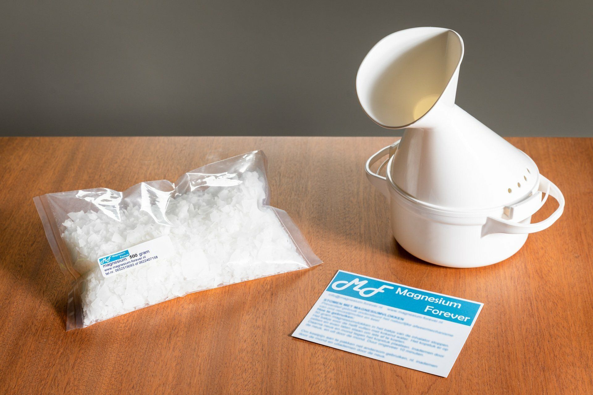 Op een houten tafel liggen een witte gezichtsstomer, een zakje witte kristallen en een gebruiksaanwijzing.