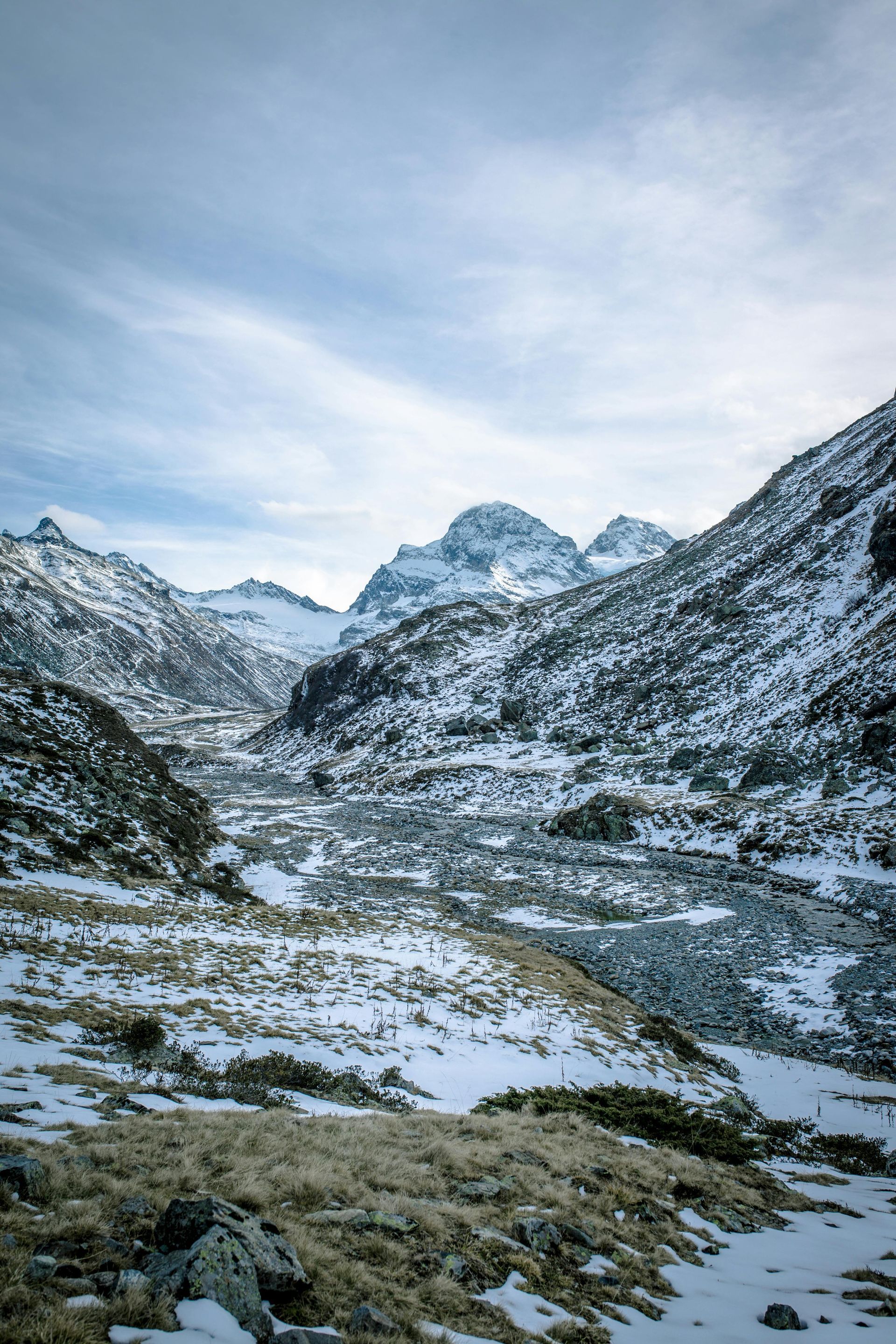 Een met sneeuw bedekt dallandschap leidt naar ruige, met ijs bedekte bergtoppen onder een heldere, bewolkte hemel.