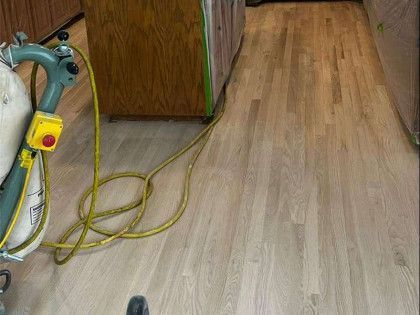A floor sanding machine sits on light wood flooring next to a cabinet, preparing to sand the floor.