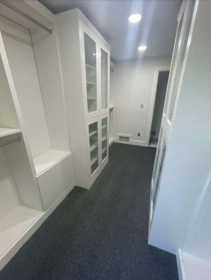 White custom closet with glass-front cabinets and built-in bench. Dark gray carpet and white walls.
