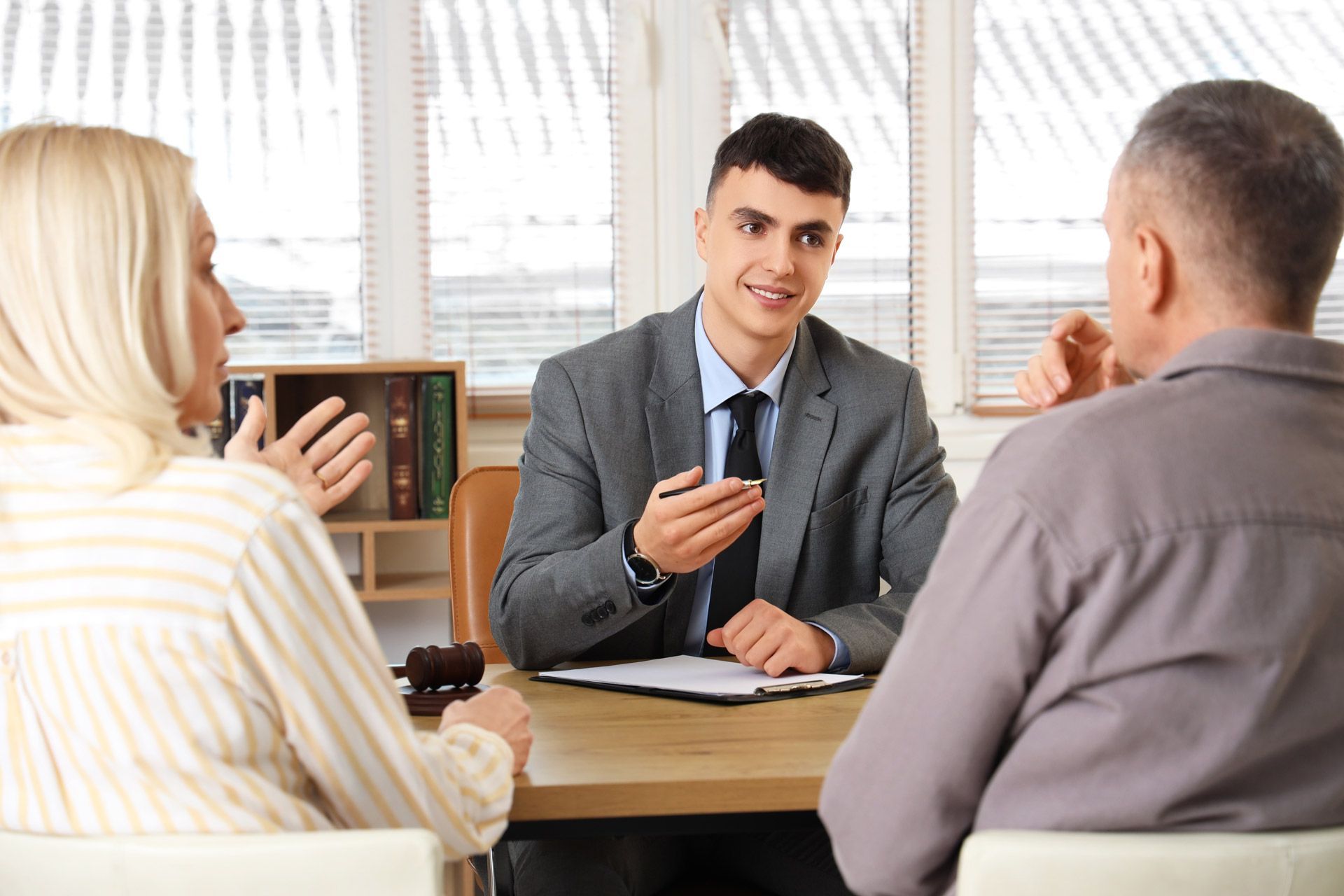 An attorney in a gray suit discusses legal matters with a couple seated across a desk with a gavel