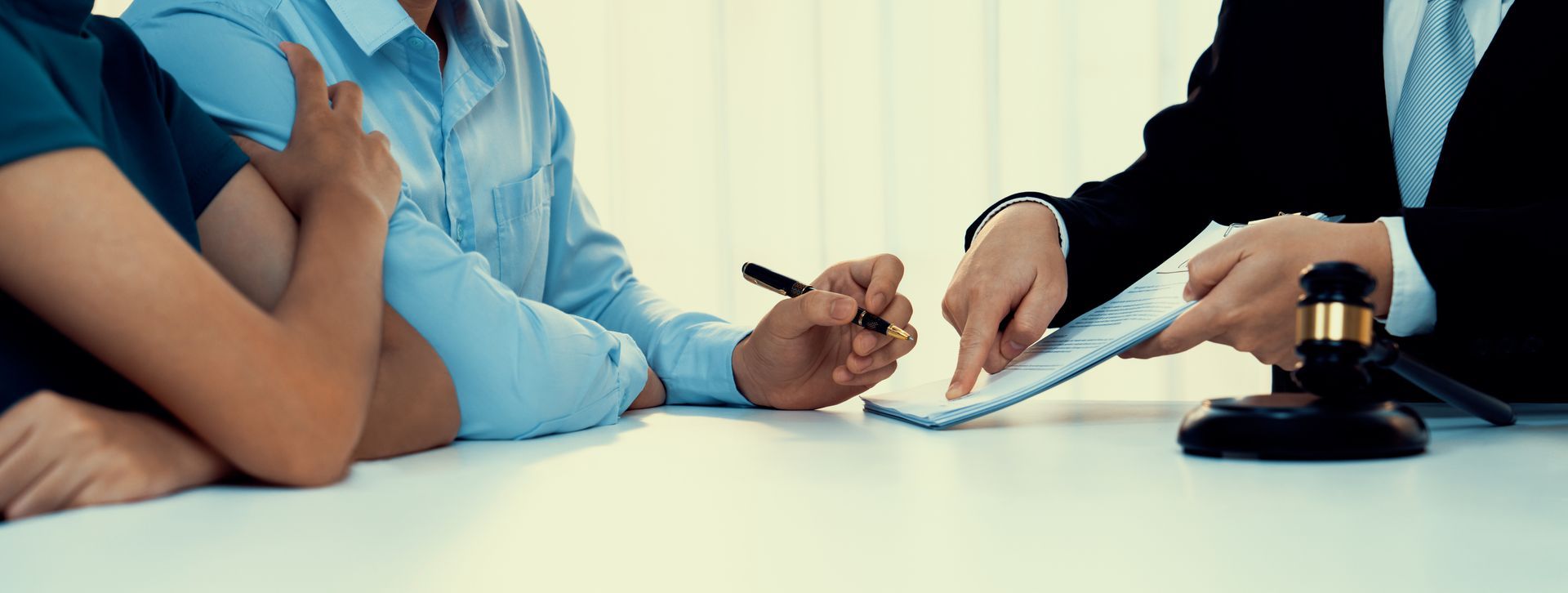 A legal consultation with two clients on the left and a lawyer on the right pointing at a document.