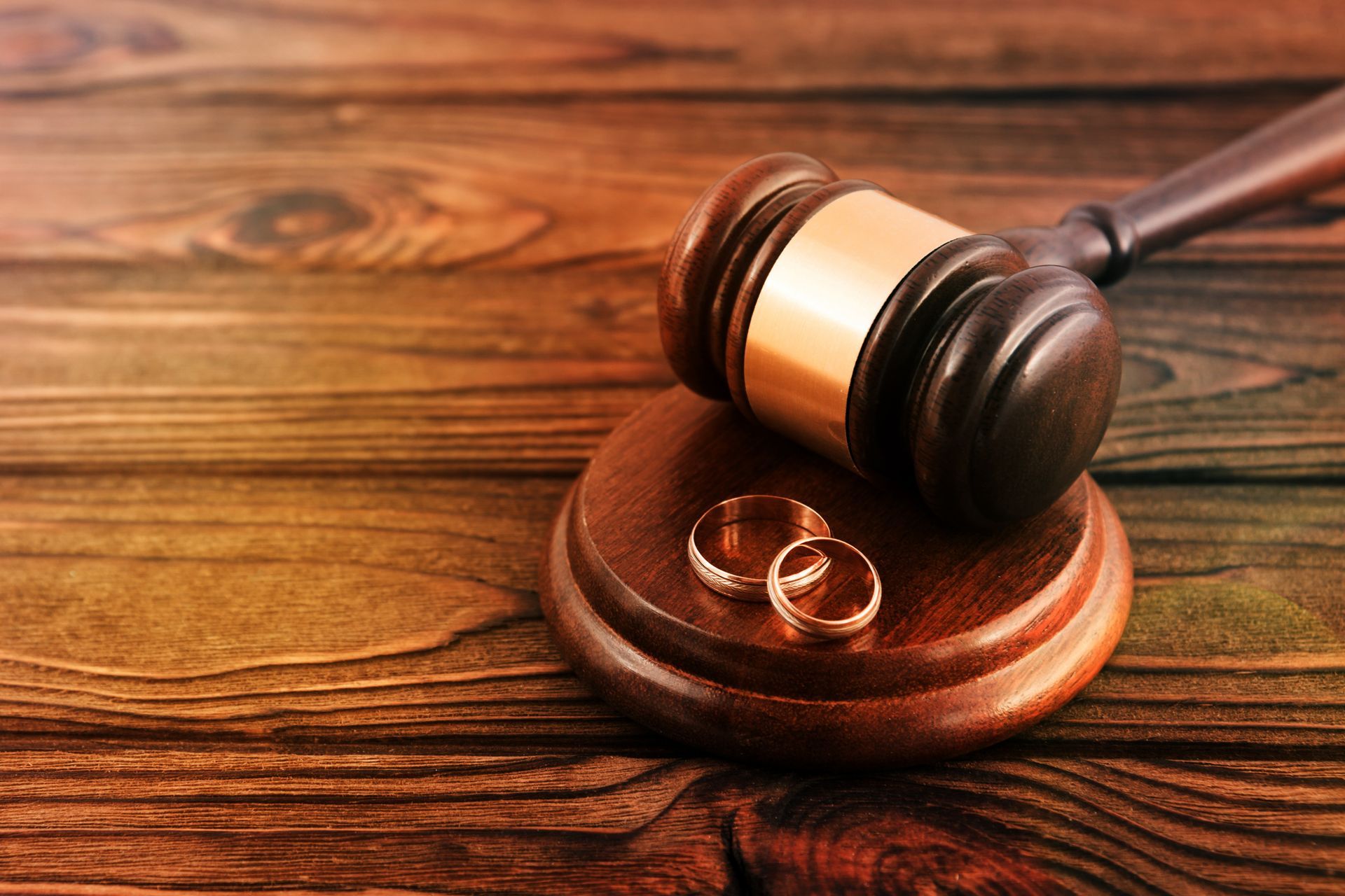 A pair of gold wedding rings, on a divorce attorney's wooden hammer, over a desk.