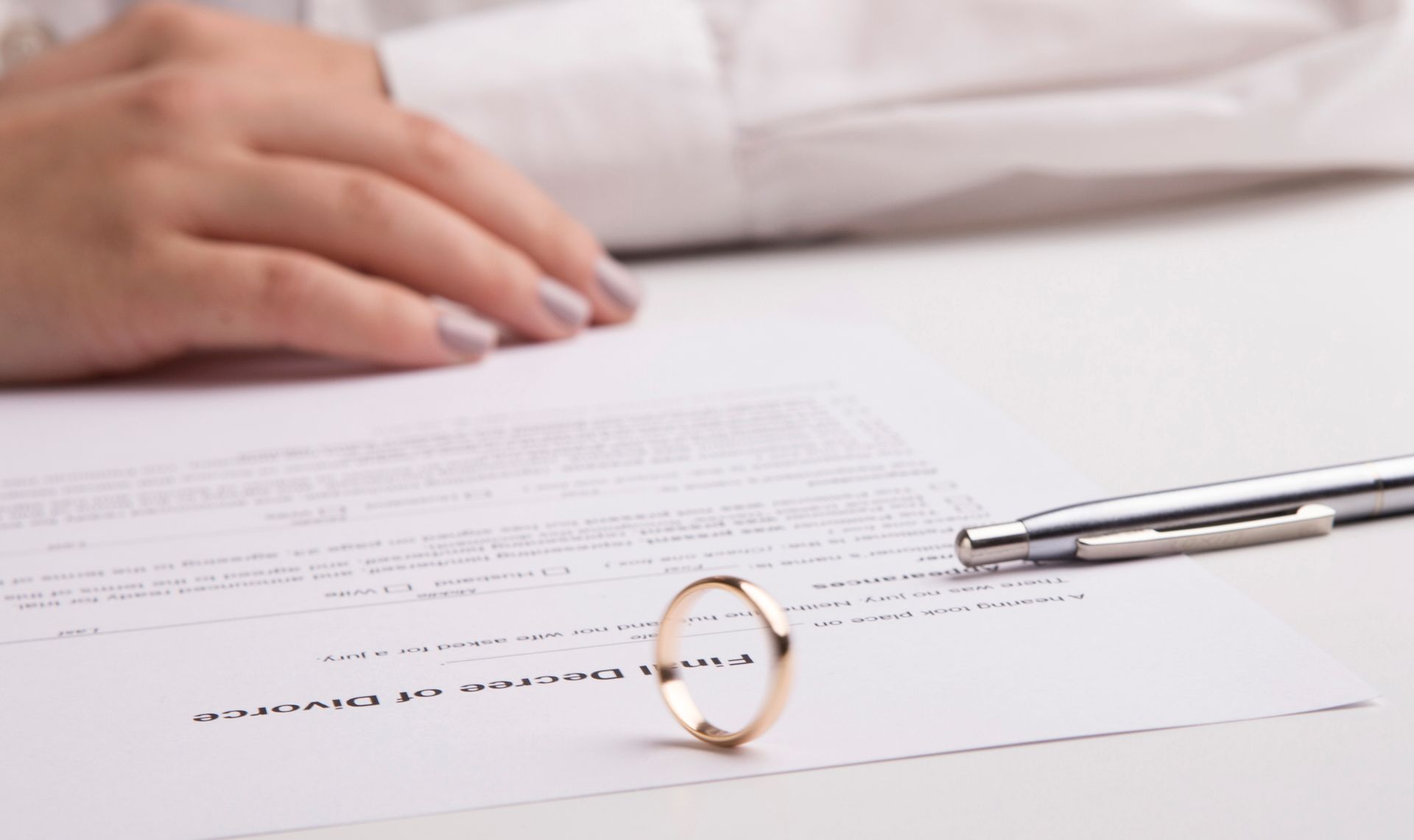Close-up of a hand near final divorce papers and ring from a divorce attorney's desk.