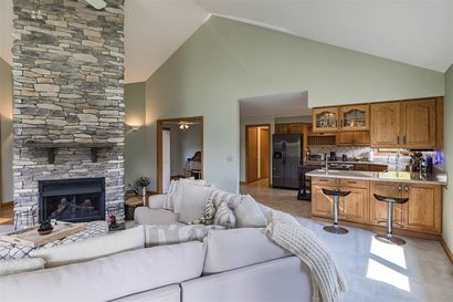 A kitchen with white cabinets , wooden floors , stainless steel appliances and a large island with chairs.