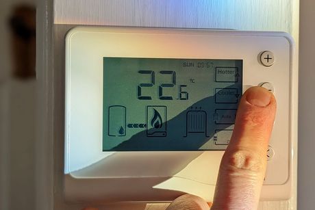 A person is pressing a button on a thermostat.