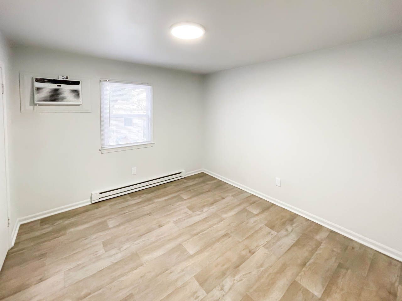 An empty bedroom with hardwood floors and a window.