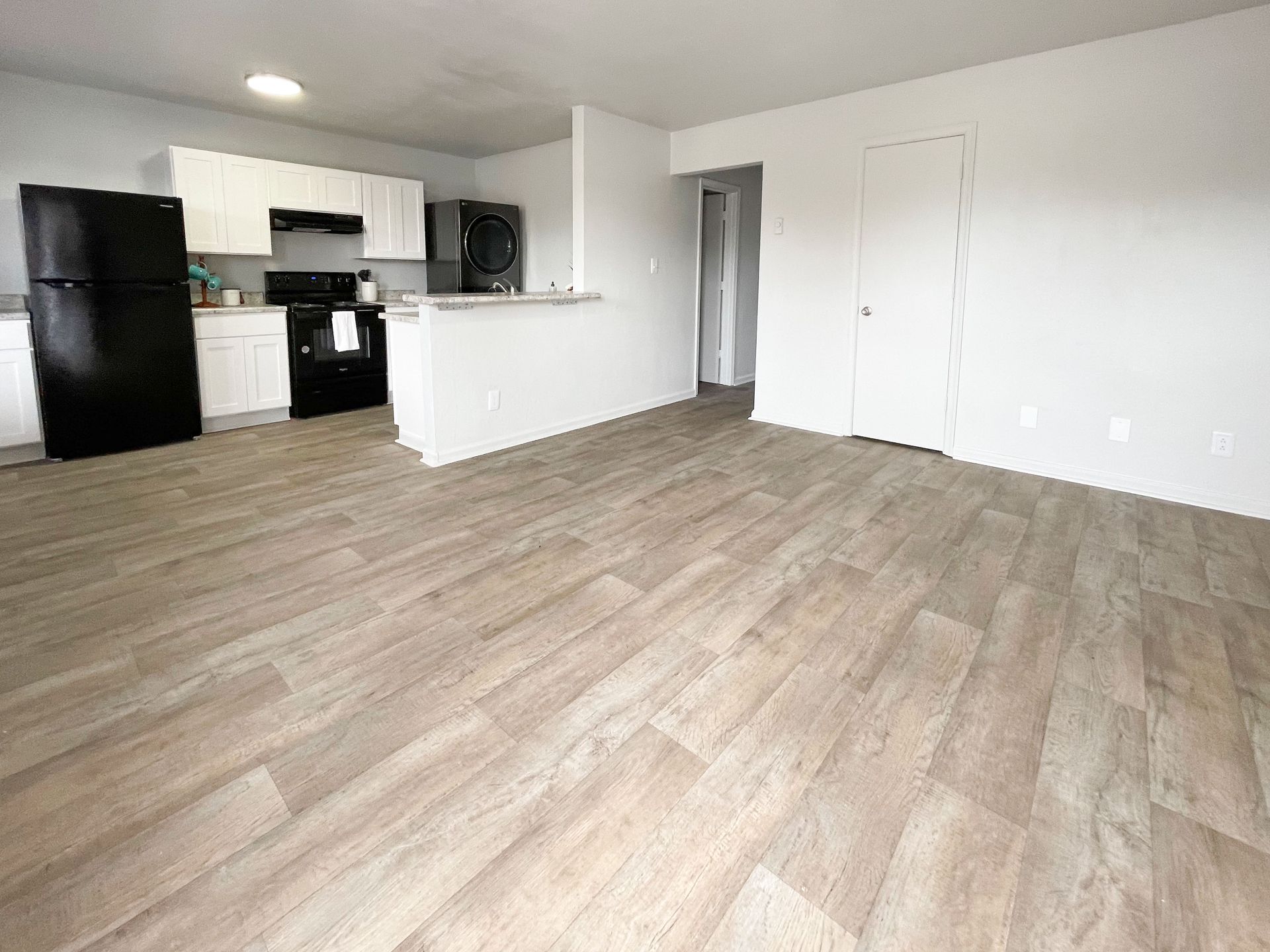 A living room with hardwood floors and a kitchen in the background.