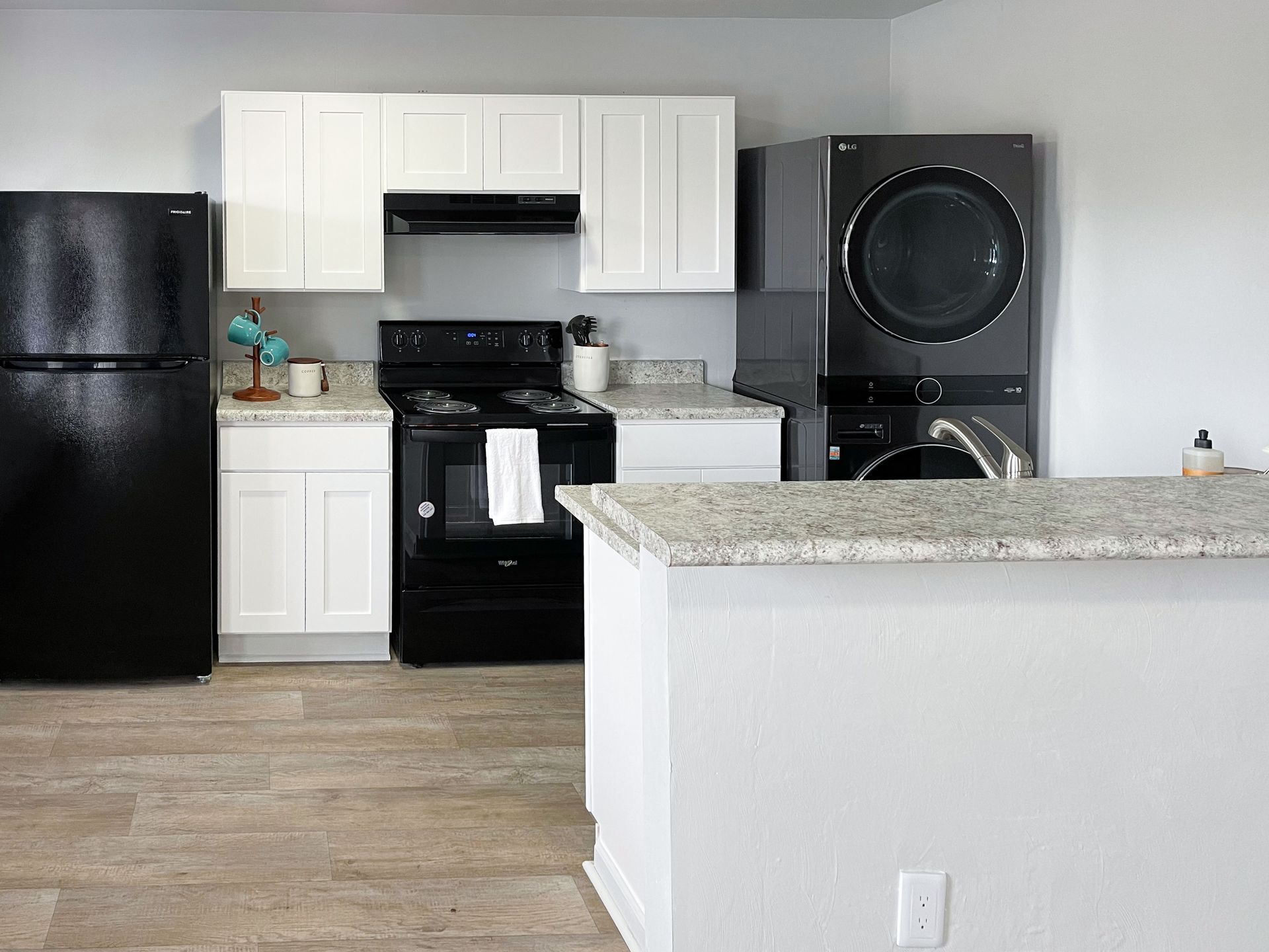 A kitchen with a black refrigerator , black stove , black washer and dryer , and white cabinets.