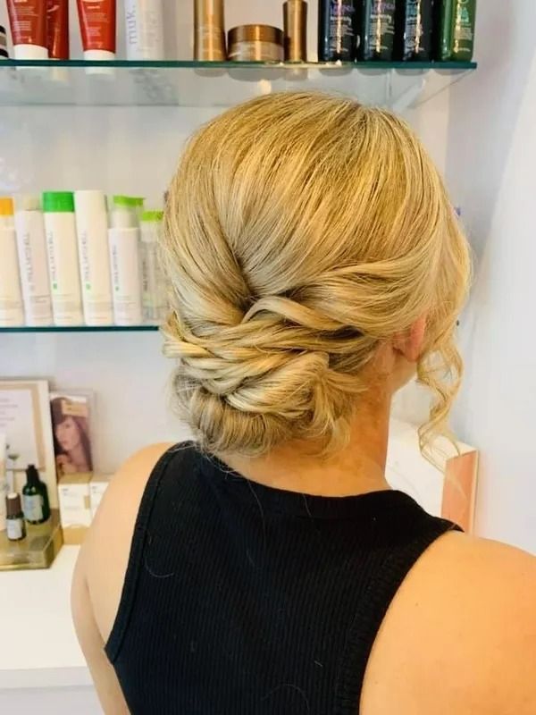 Woman With Blonde Updo Hairstyle, Black Top, in a Salon Setting With Shelves of Products — Artistry Of Hair in Redlynch, QLD