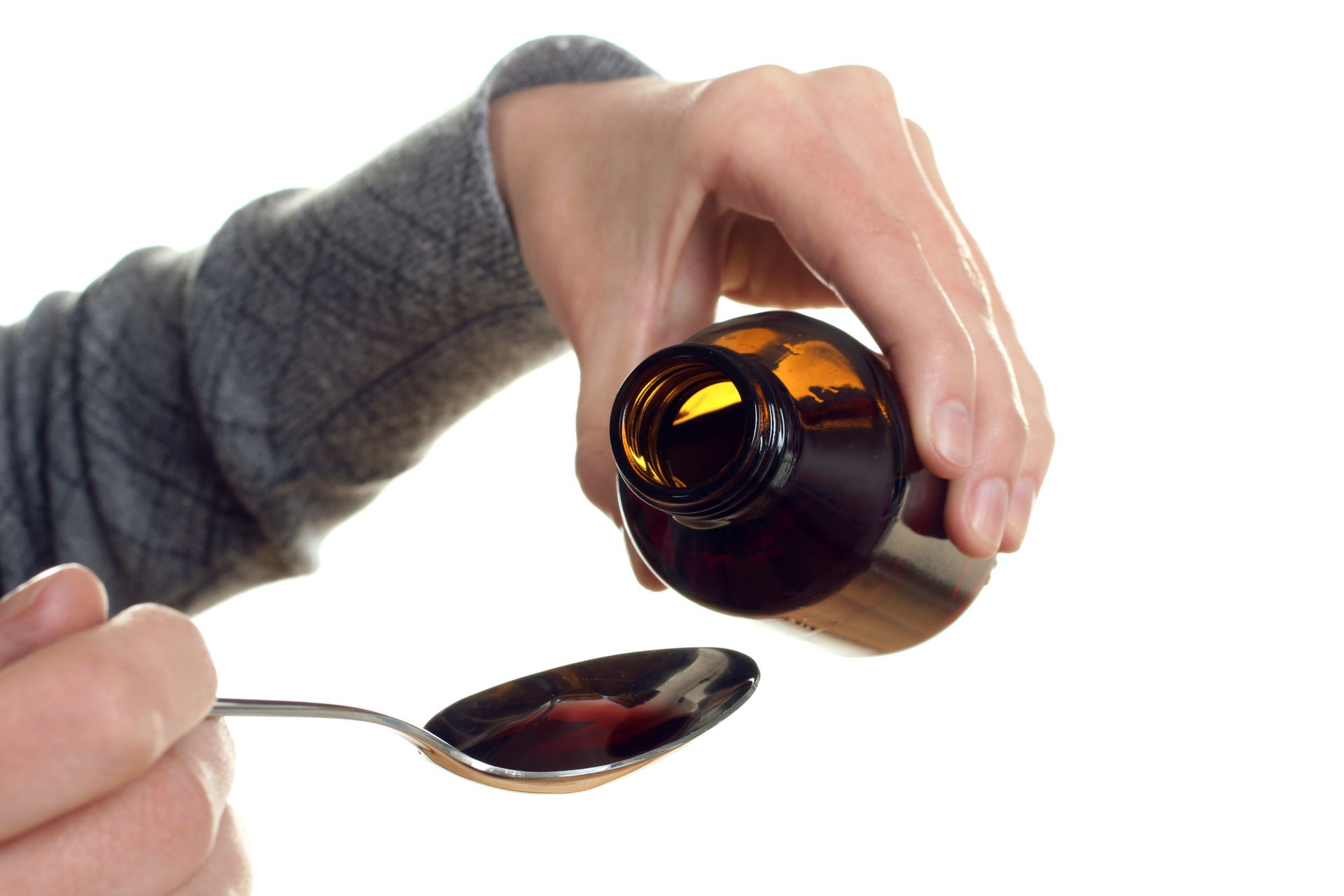 Hand pouring liquid medicine from a brown bottle into a spoon
