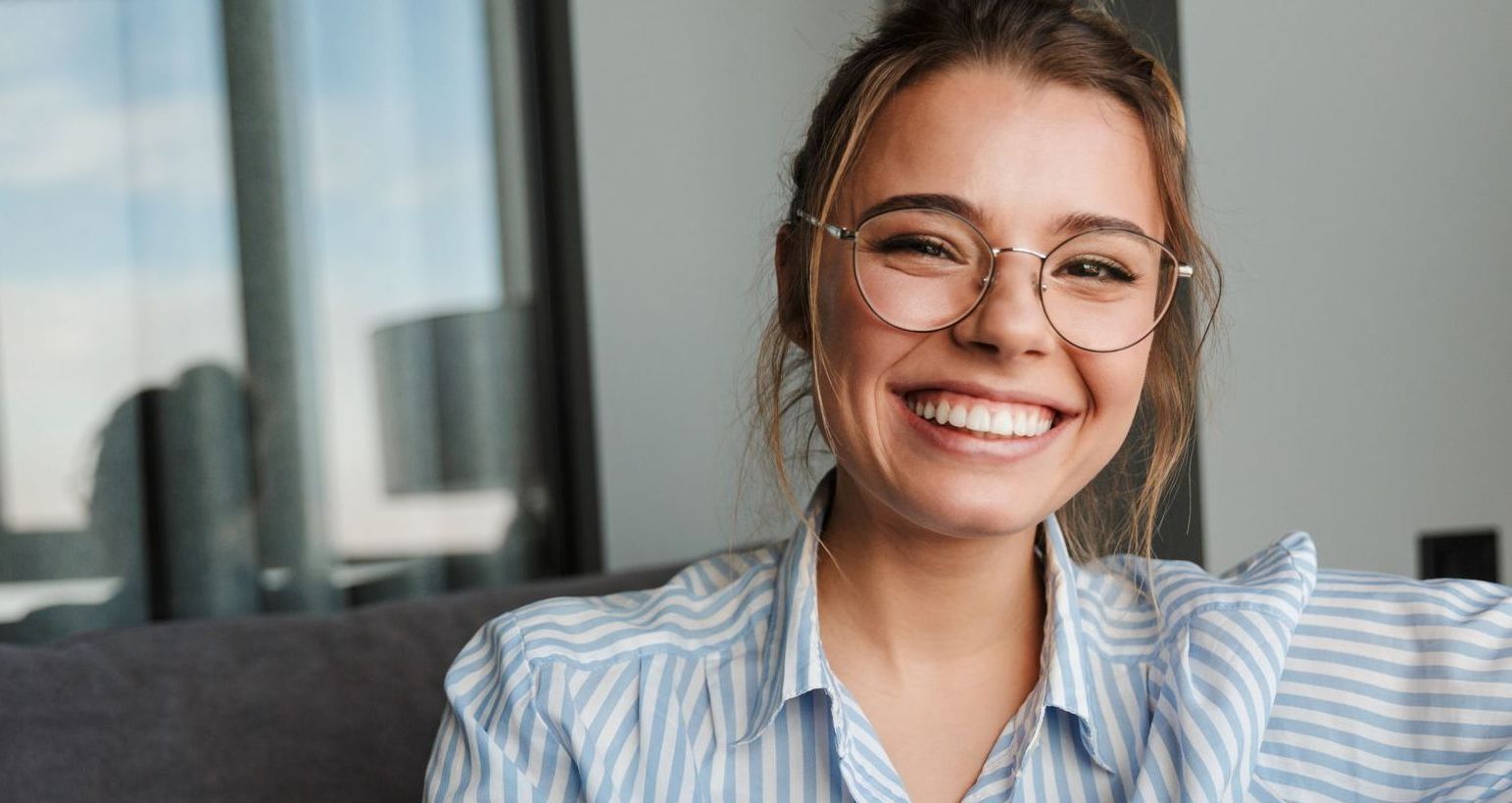 A woman wearing glasses is smiling while sitting on a couch.