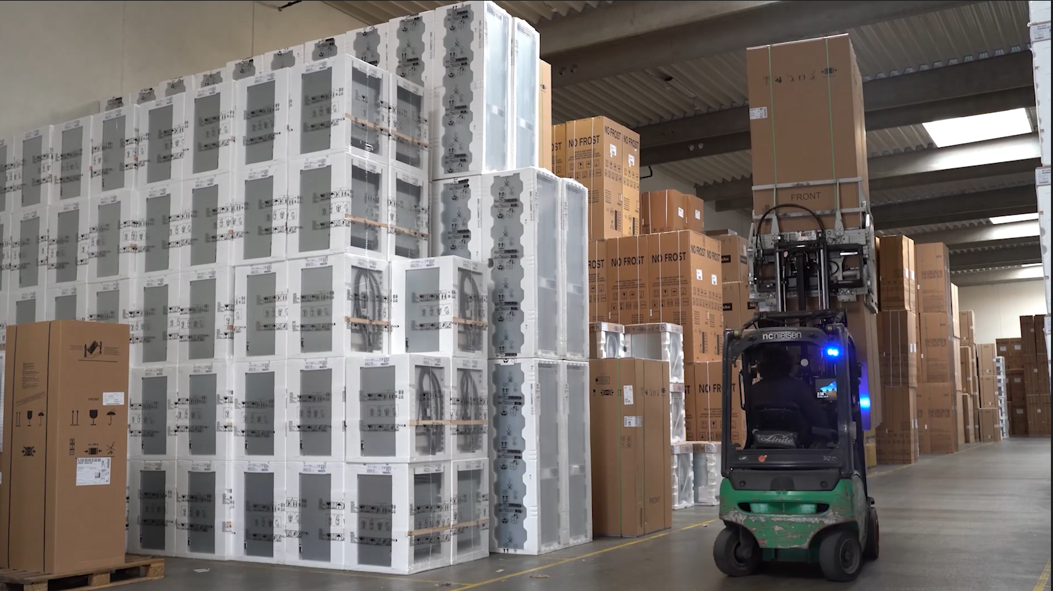 Forklift in warehouse transporting boxes. Large stacks of boxes in background.