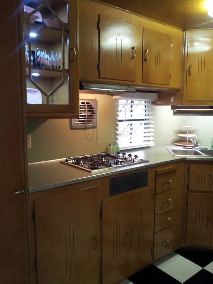 Kitchen in a vintage camper with wood cabinets, stove, sink, and checkered floor.