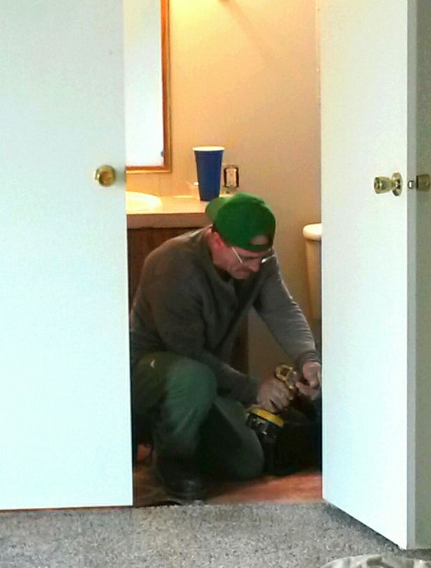Construction worker in a hard hat on a ladder, inspecting the ceiling inside a room.