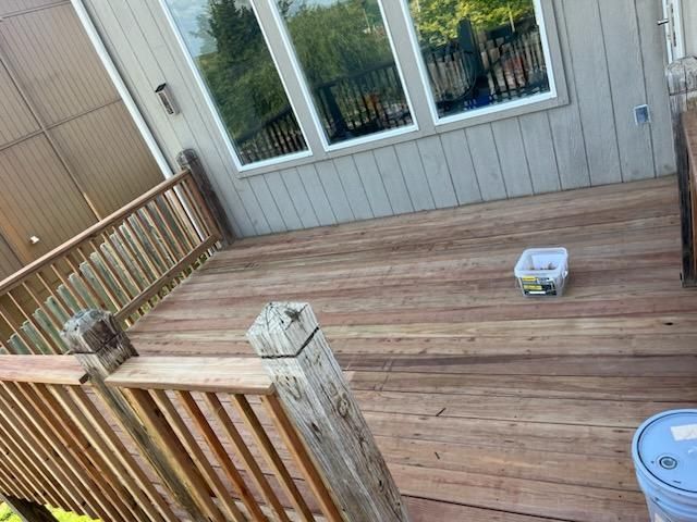 Wooden deck with handrails and windows on a house exterior. A bucket and tool container are present.