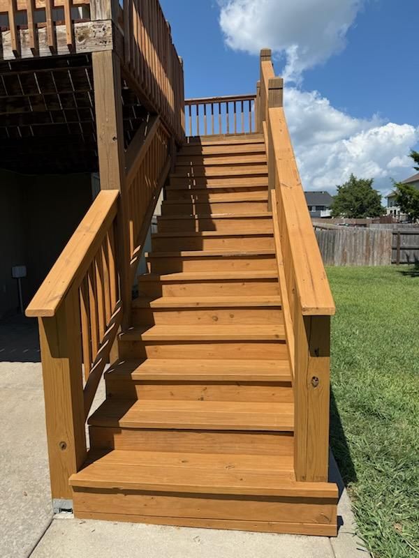 Wooden outdoor staircase leading up to a deck, set against a lawn and blue sky.