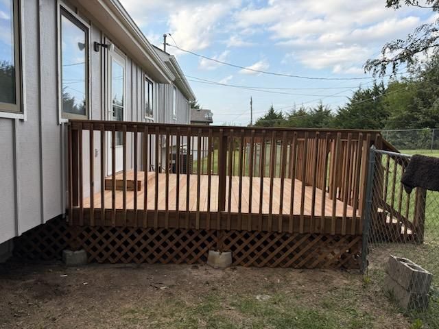 Wooden deck with railing attached to a white house, on a grassy yard.